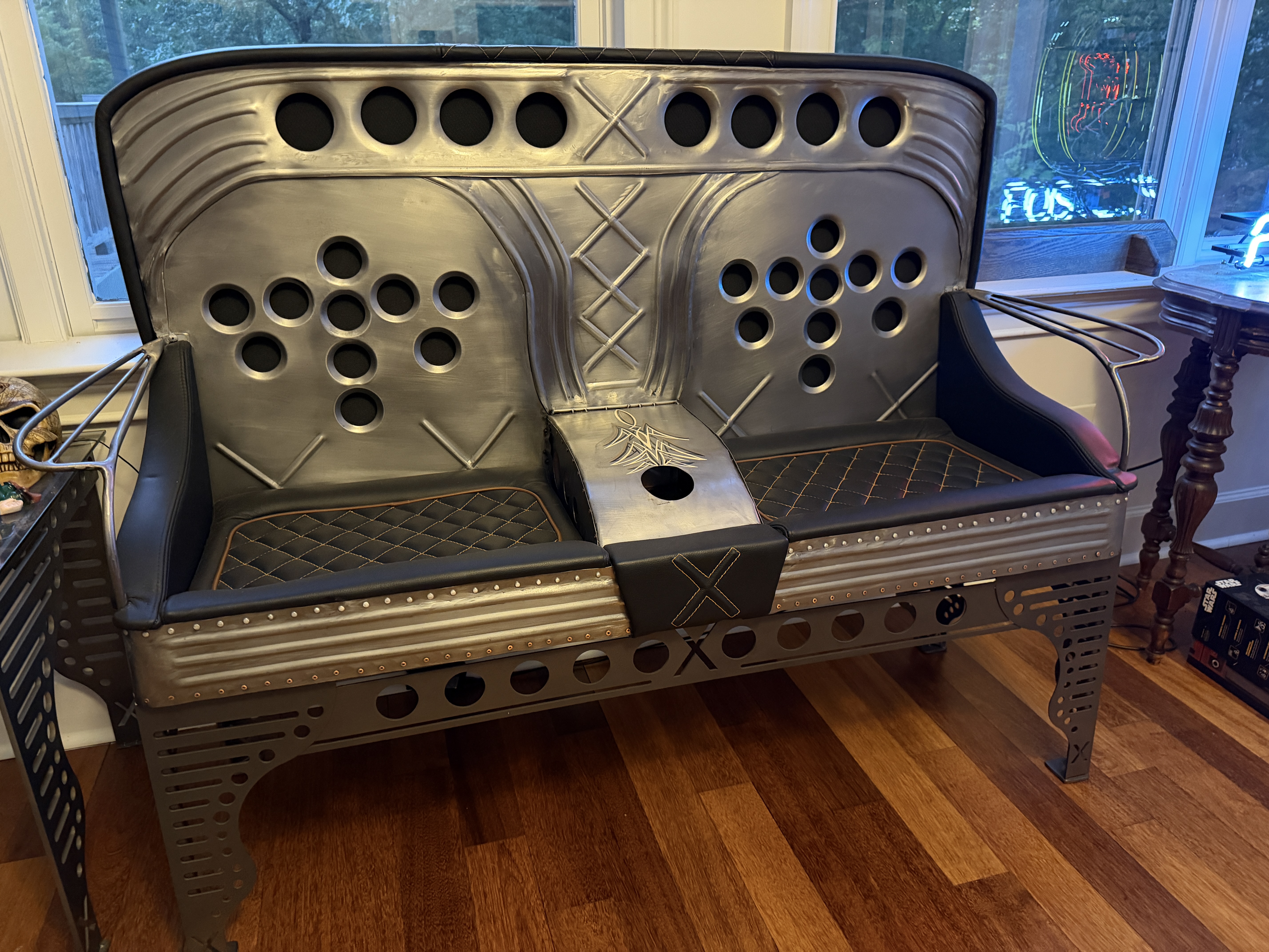 A two-seat couch built from steel with circular perforated back panels, diamond-stitched leather cushions, and the X mark on the center console.